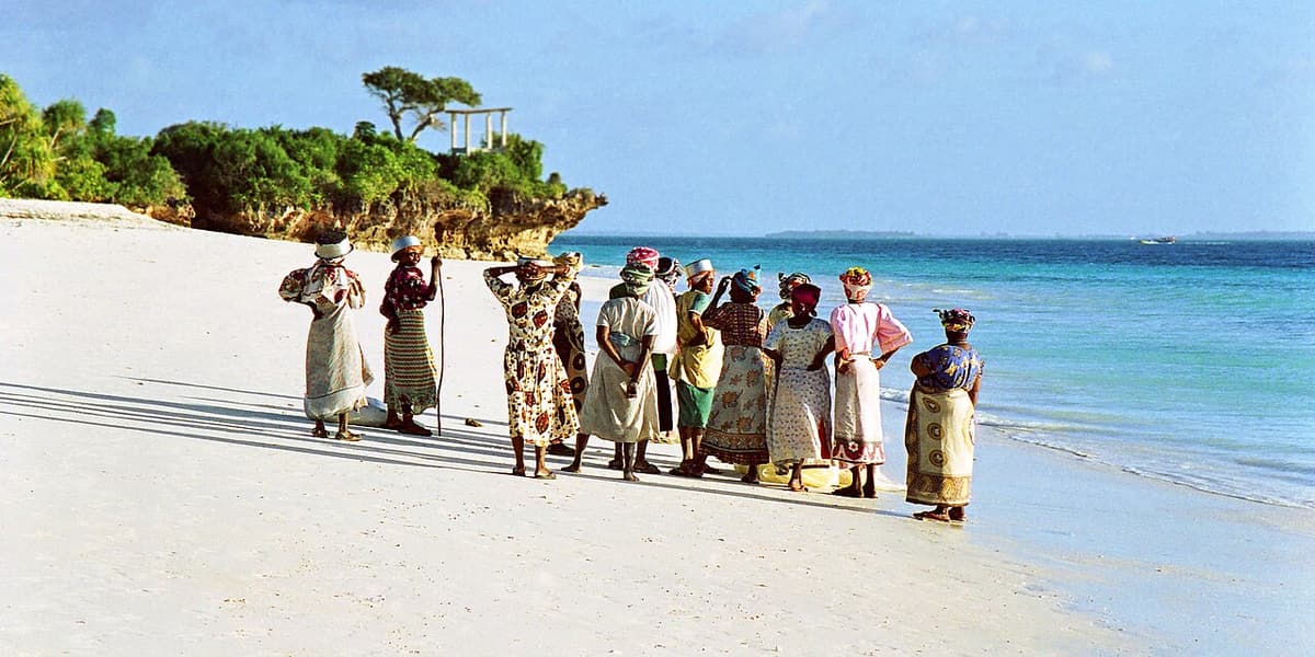 Women in colourful kangas walking along the beach at Nungwi